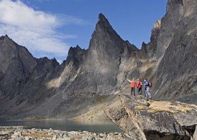 three people standing on a rock, jagged mountains in the background