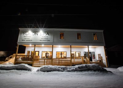 white, wooden building on a snow-covered road at night