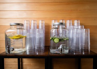 lemon and cucumber infused water in a jug, multiple stacked drinking glass